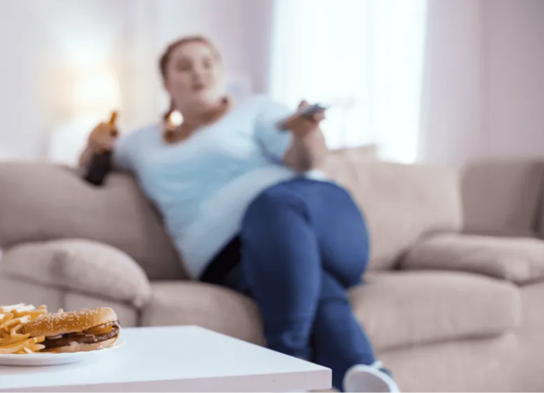 ragazza sullo sfondo sovrappeso che guarda la tv mentre mangia un hamburger e beve birra
