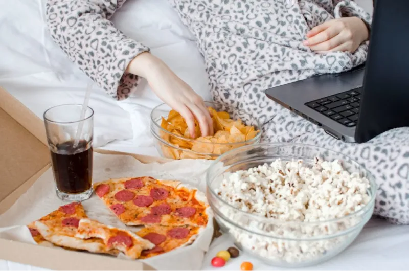 Persona che mangia pizza, popcorn e patatine davanti al pc
