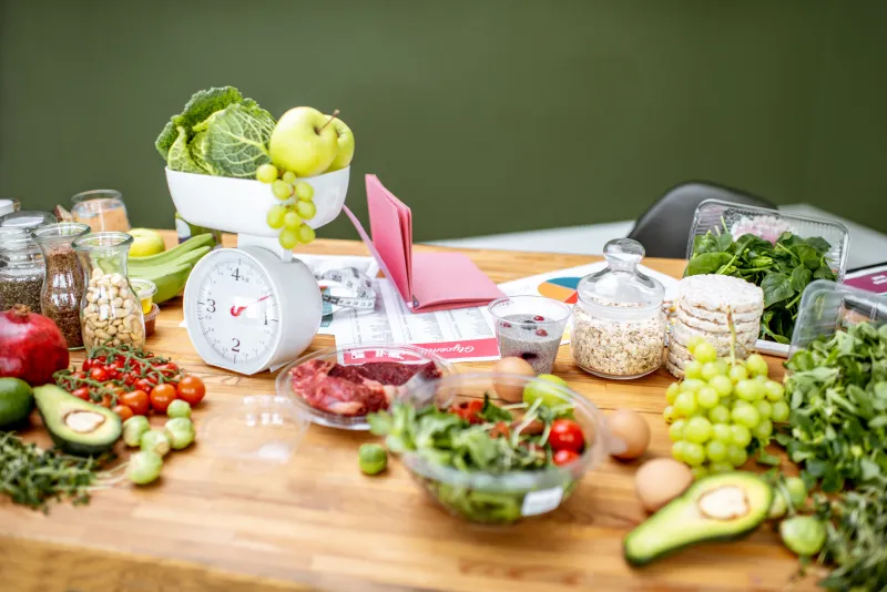 Tavolo di un nutrizionista, pieno di cibi freschi e di una bilancia analogica