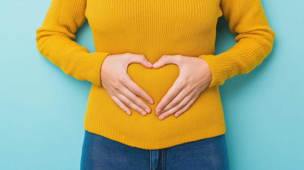 Donna che disegna un cuore con le mani sulla pancia.