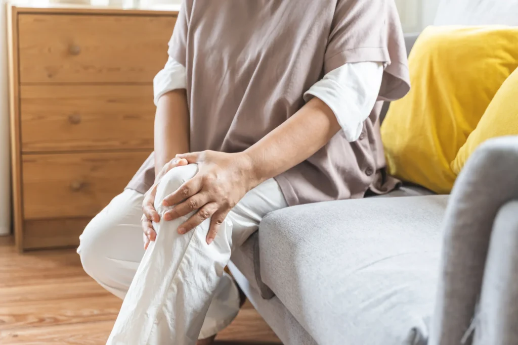Signora seduta sul divano che si tiene un ginocchio.