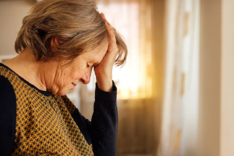 Anziana si tocca la fronte con la mano.