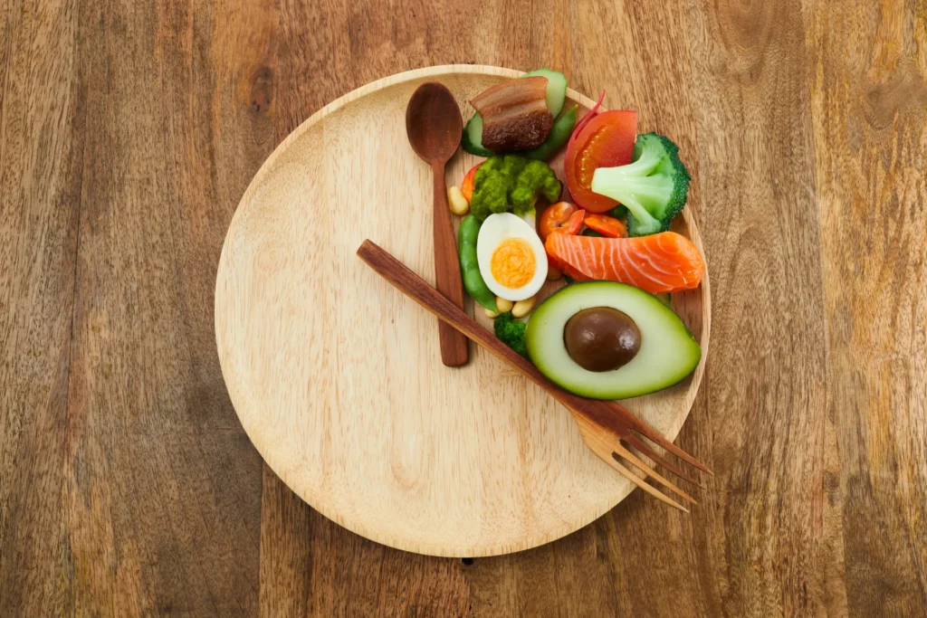 Piatto in legno con alimenti proteici e verdure disposti su una sola metà.